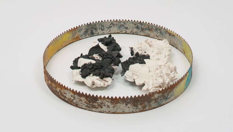 Rusty circular saw blade with black and white clay inside