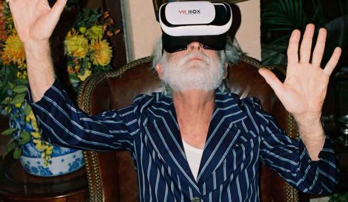 Older man wearing VR headset with hands raised