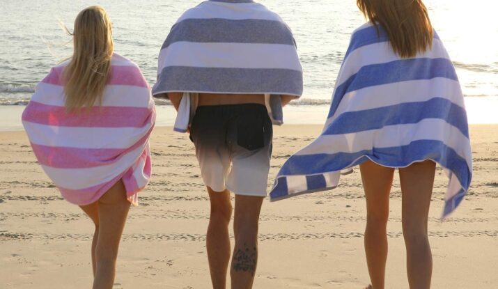 Three people wrapped in towels walking on beach