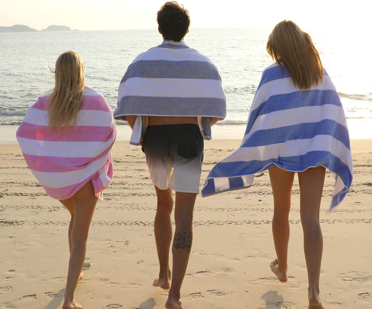 Three people wrapped in towels walking on beach