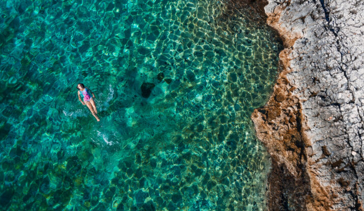 Person floating in clear turquoise water near rocky shore