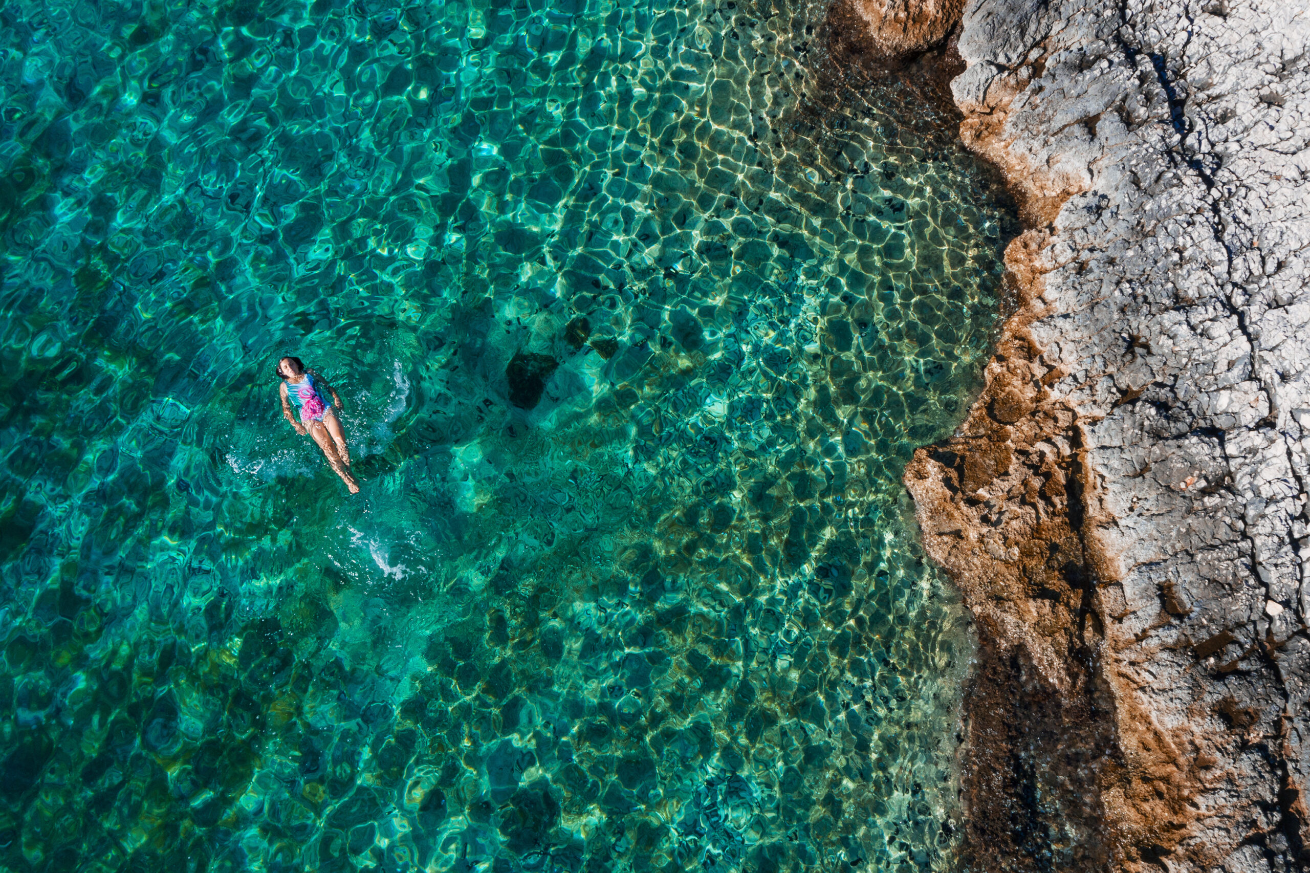Person floating in clear turquoise water near rocky shore