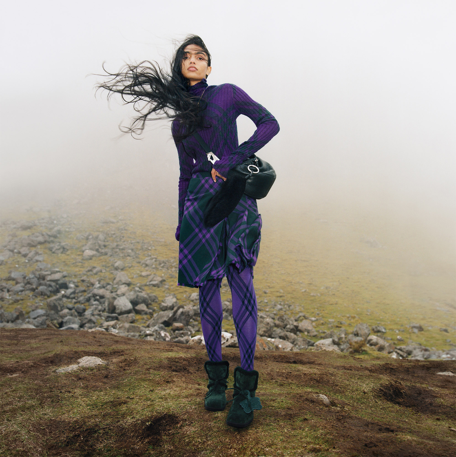 Woman in purple tartan outfit standing on rocky terrain