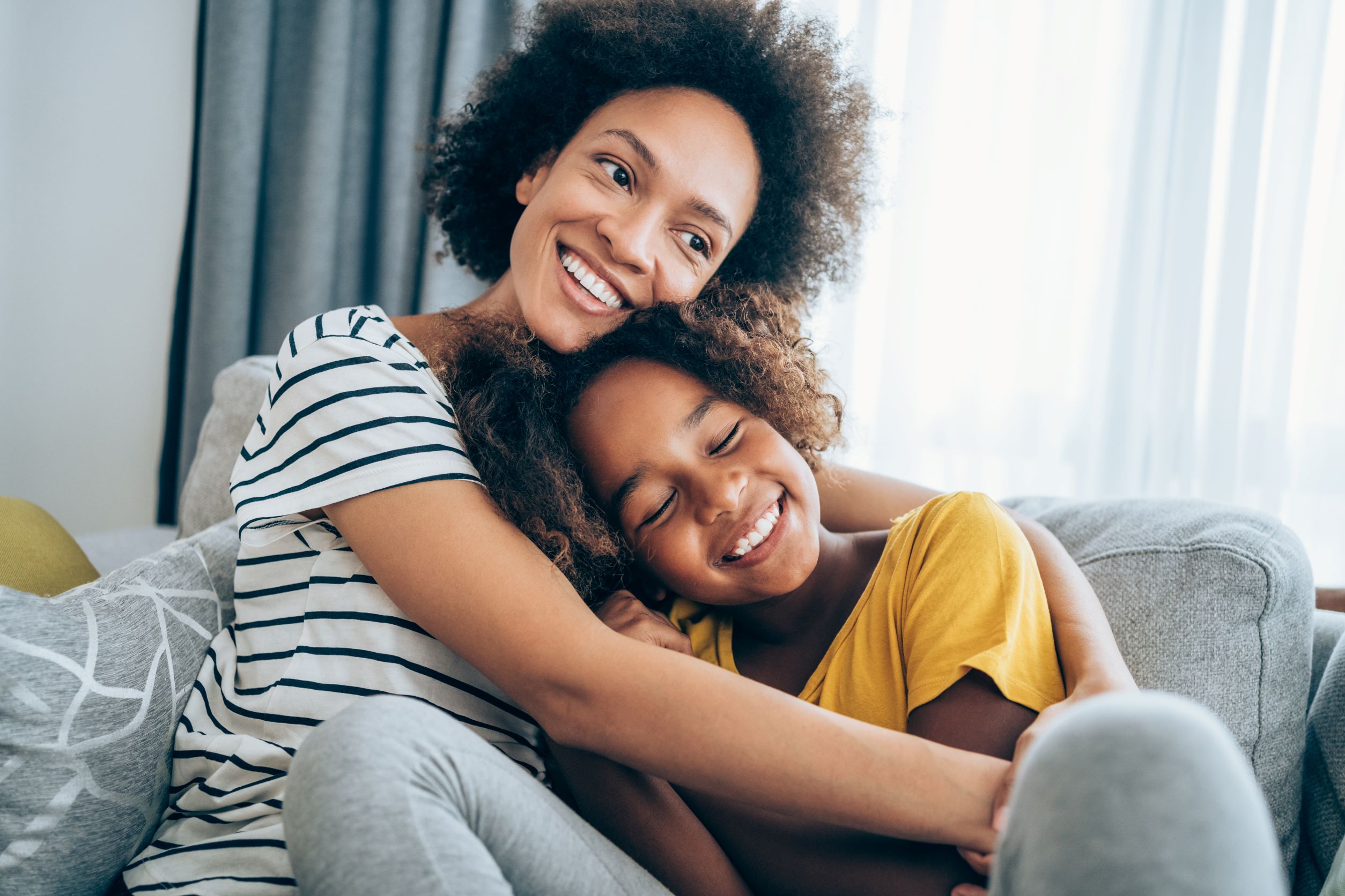 Mother and daughter hugging happily on couch