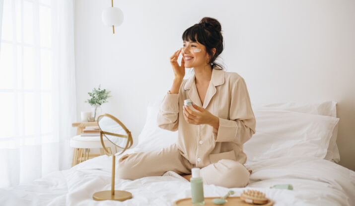 Woman in pajamas applying cream on her face