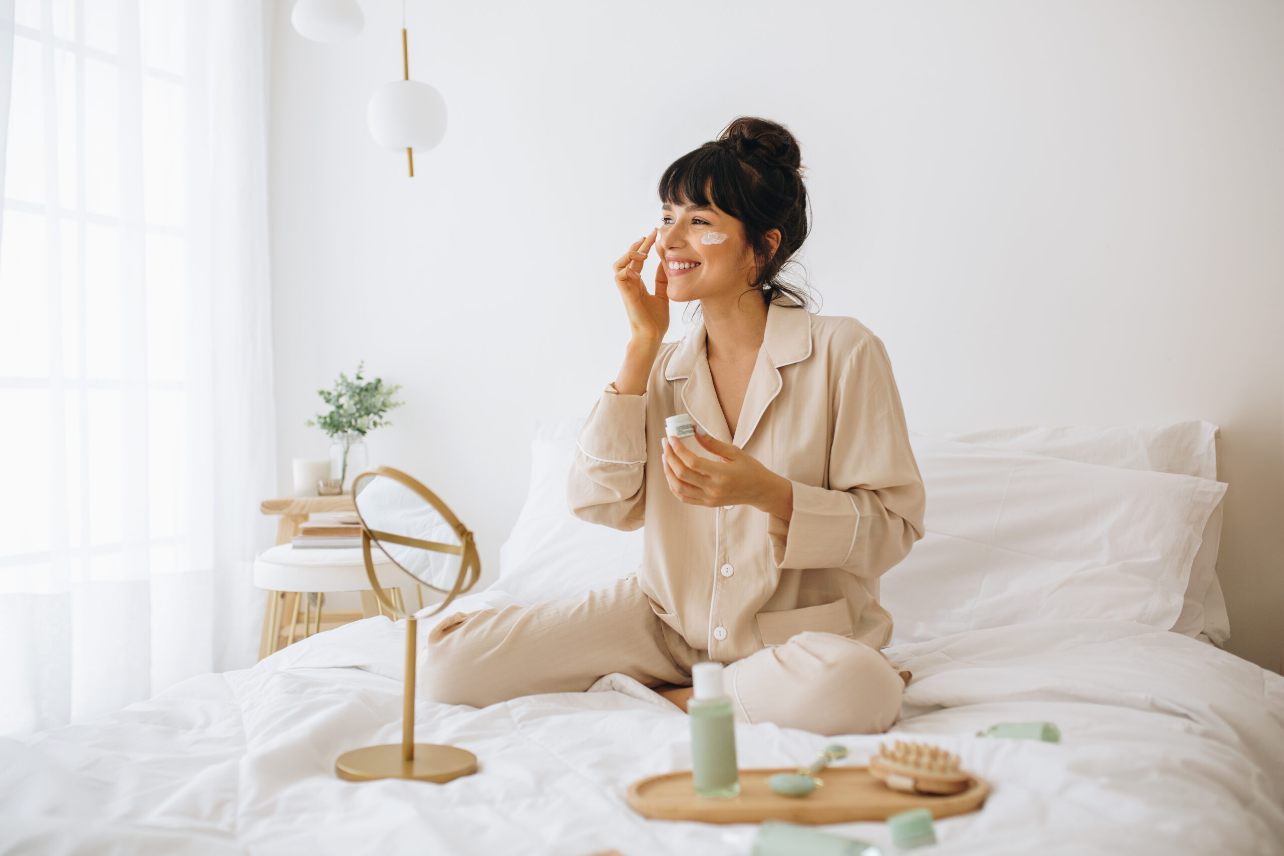 Woman in pajamas applying cream on her face