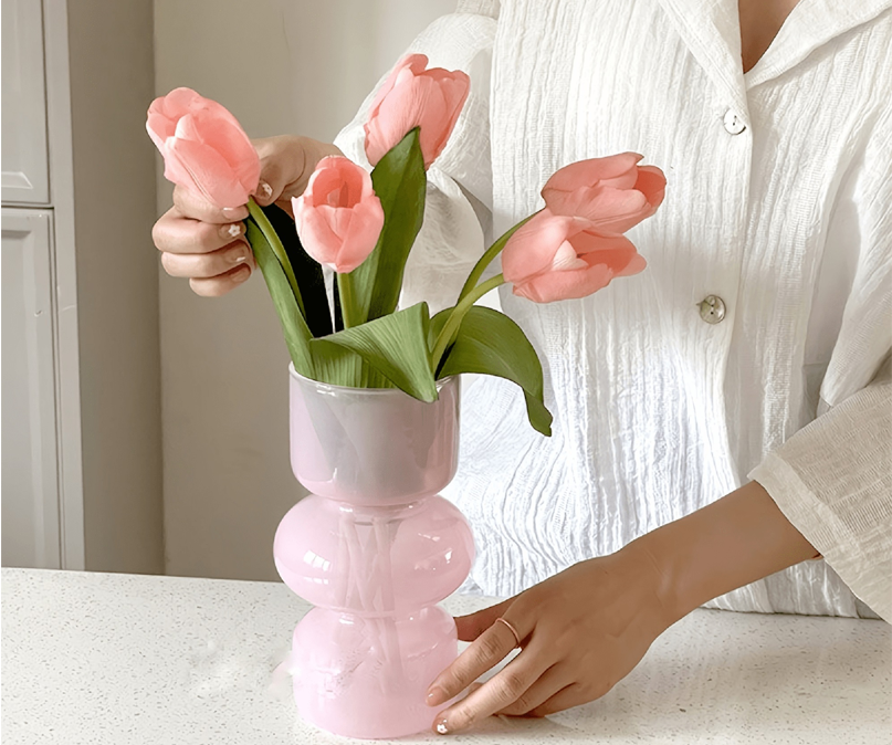 Person arranging pink tulips in translucent pink vase
