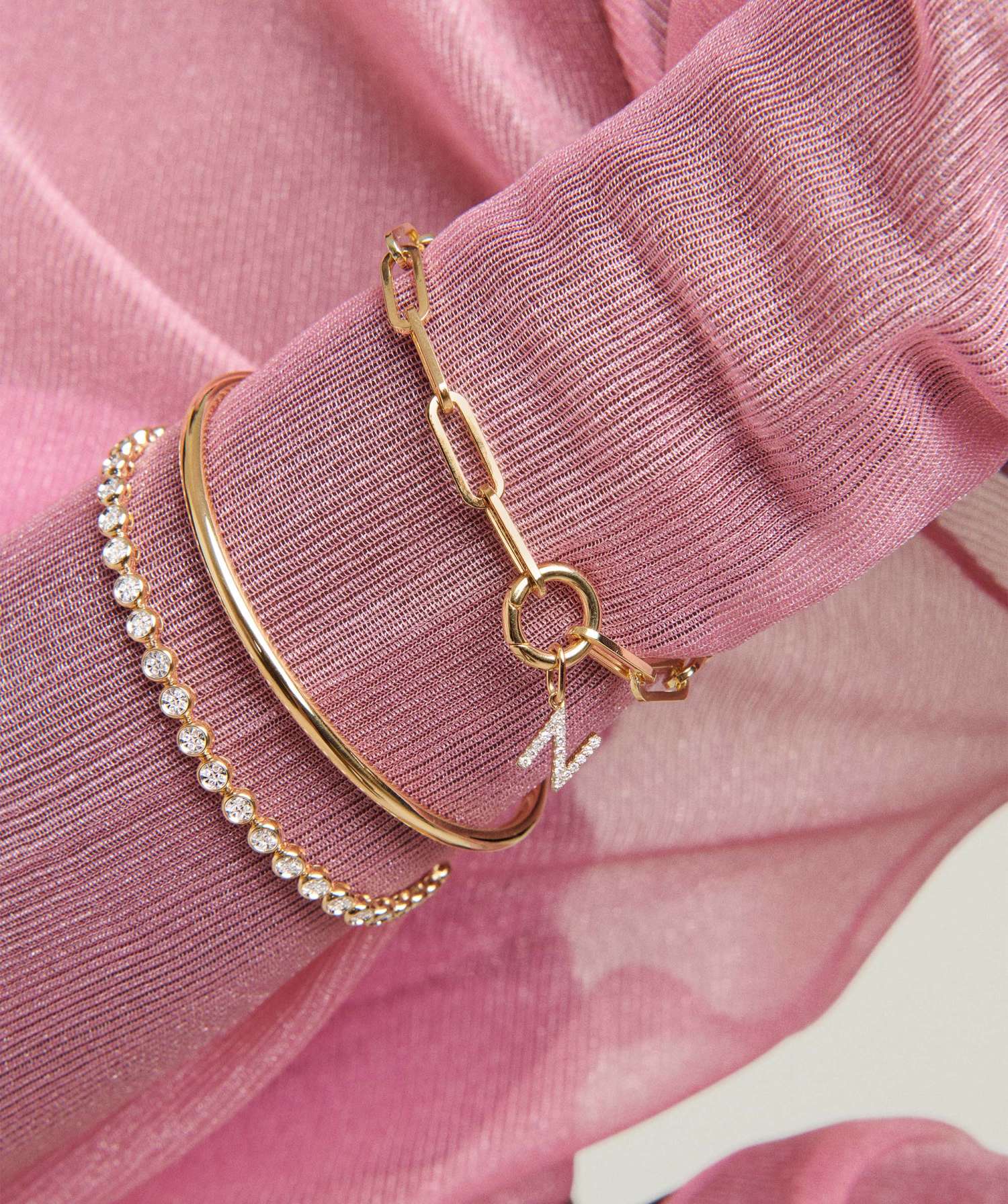 Wrist with three gold bracelets on pink fabric