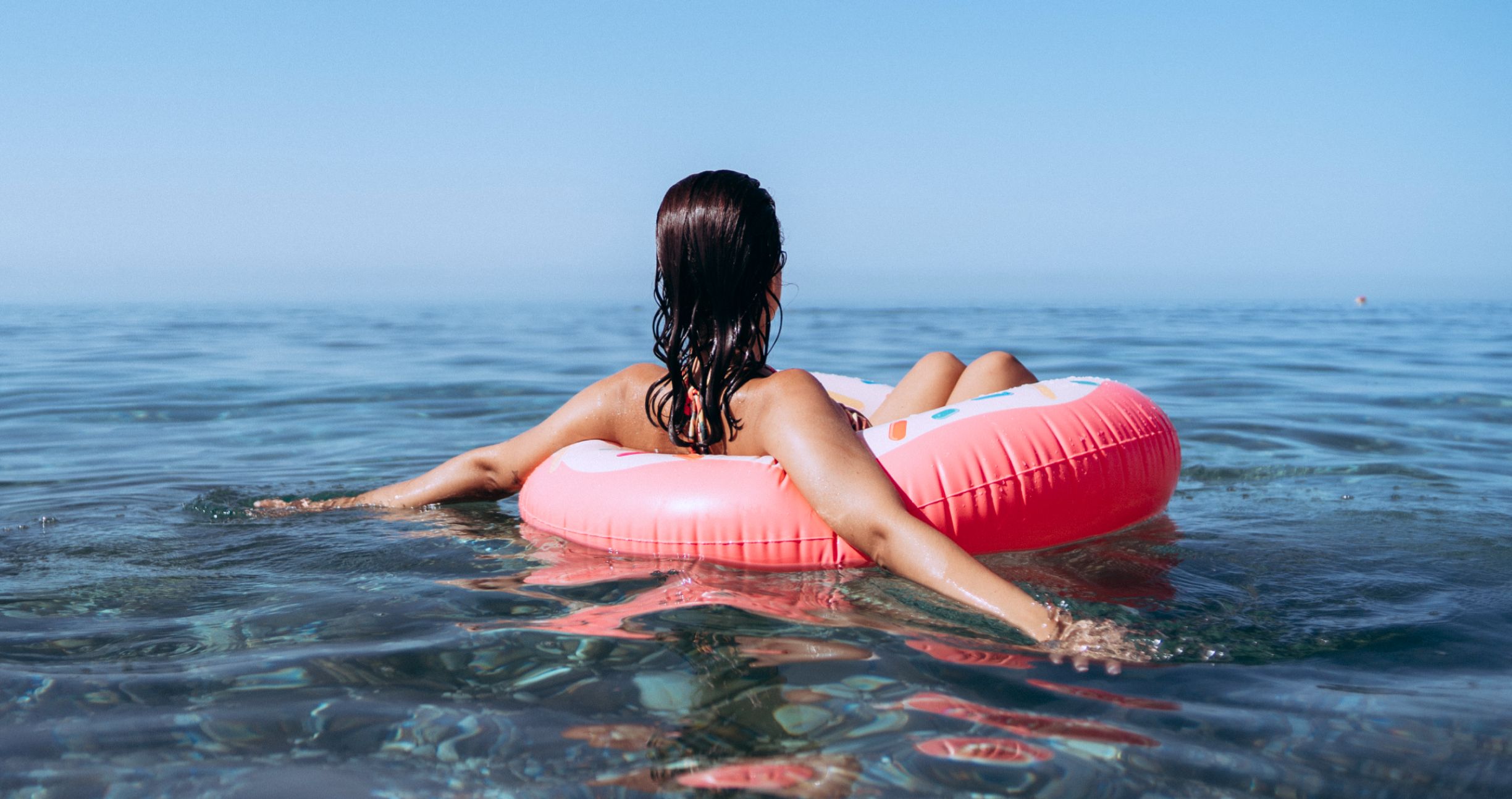 Person relaxing on pink float in clear water