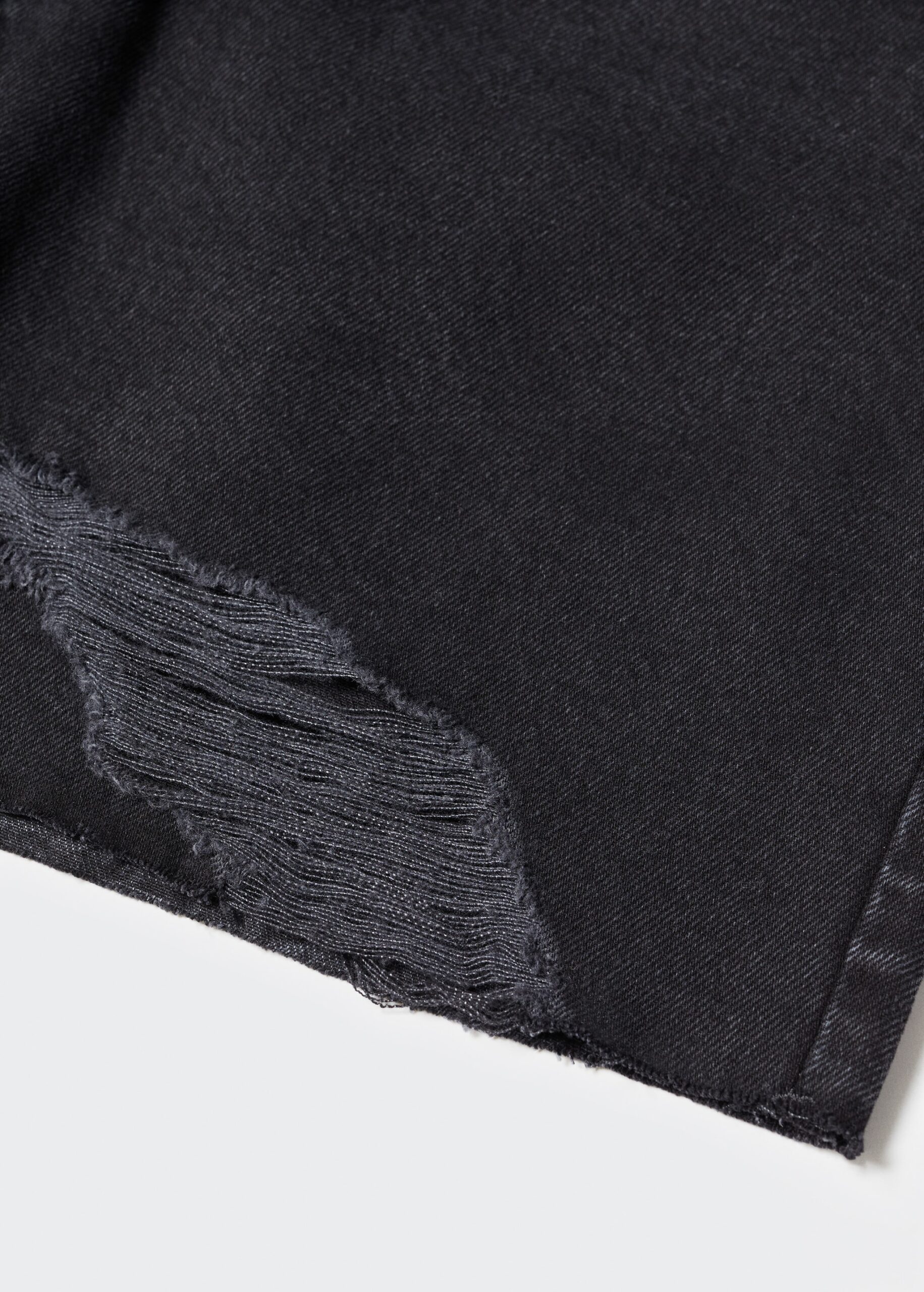 Close-up of black denim fabric with a frayed rip