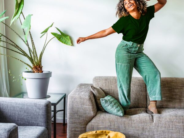 Joyful woman dancing on sofa in bright living room