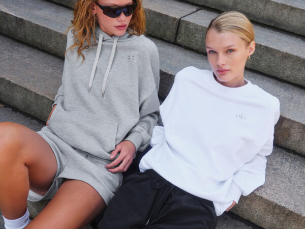 Two women wearing casual hoodies and shorts sitting on steps