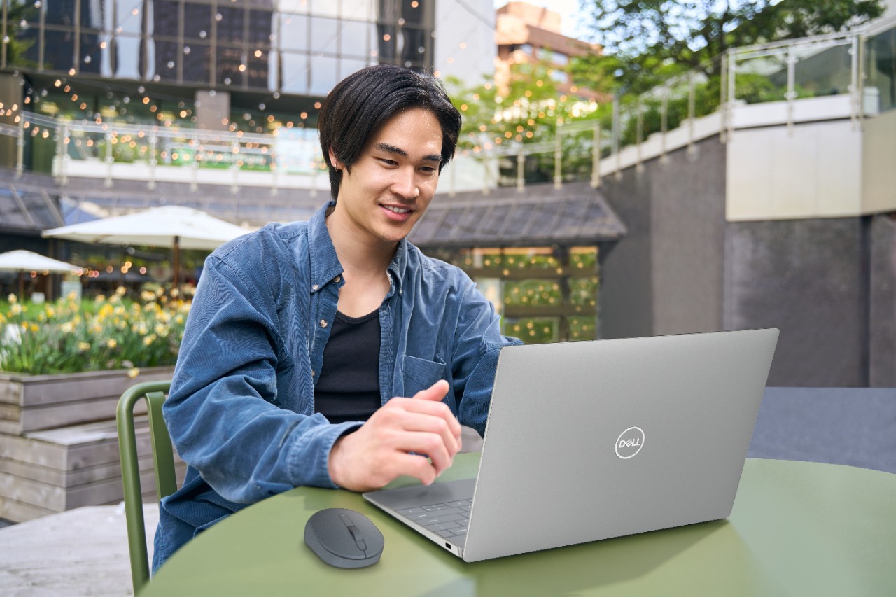 Young man using laptop outdoors at green table