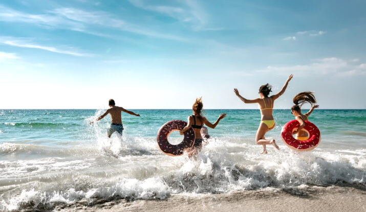 Four people jumping into ocean with inflatable rings