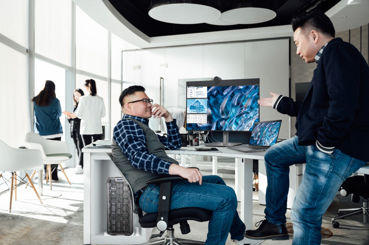 Two men discussing work at office desks with monitors