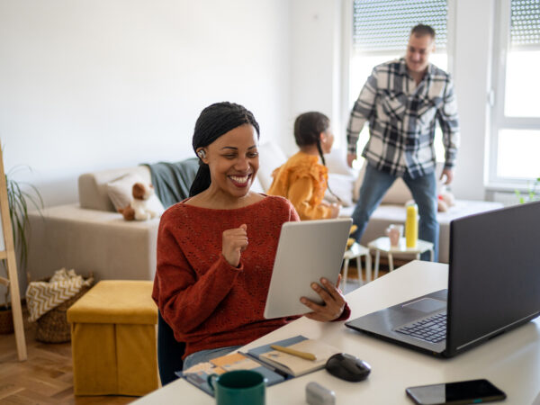 Woman smiles using tablet while family interacts behind
