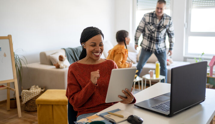 Woman smiles using tablet while family interacts behind