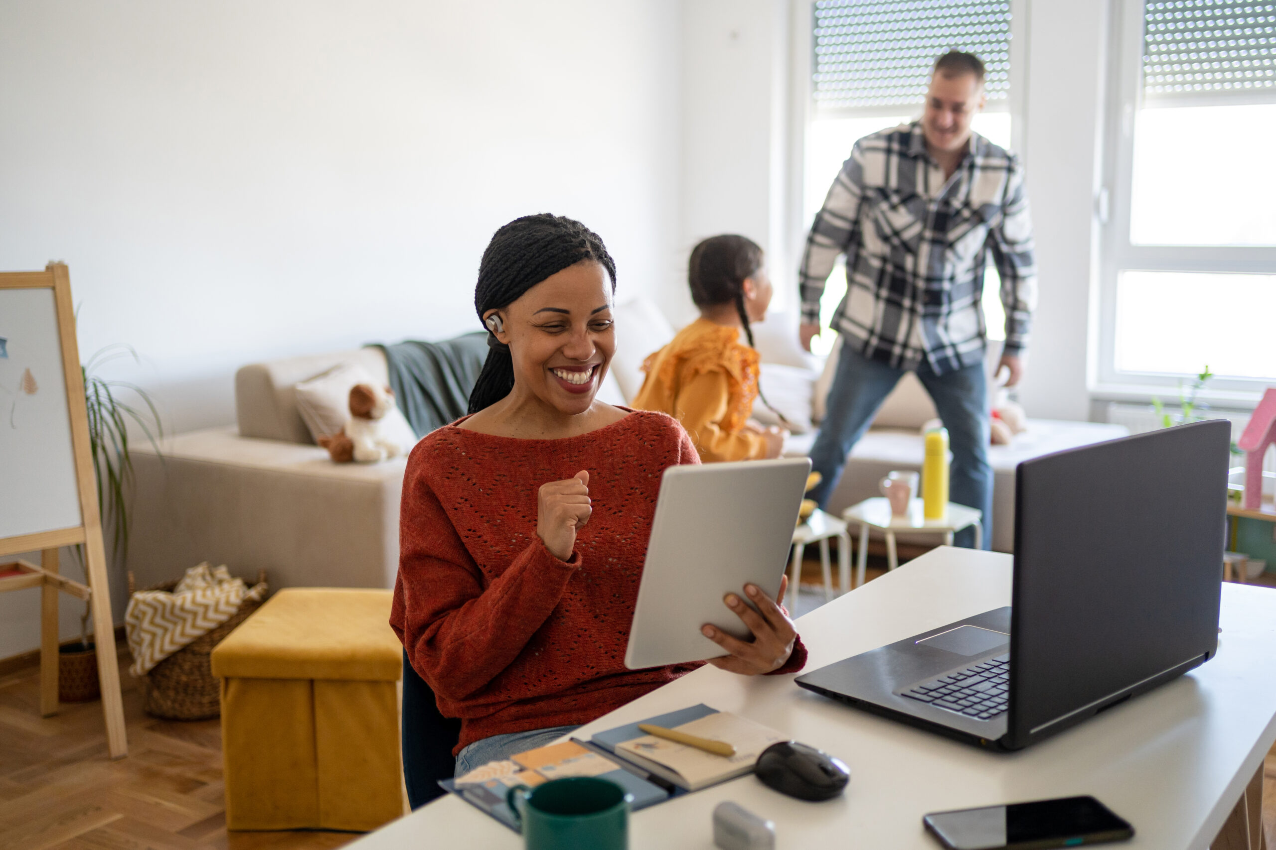 Woman smiles using tablet while family interacts behind