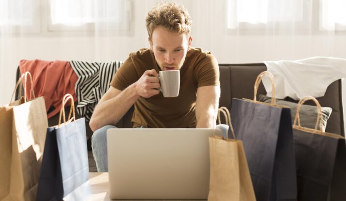 Man shopping online with coffee and bags nearby