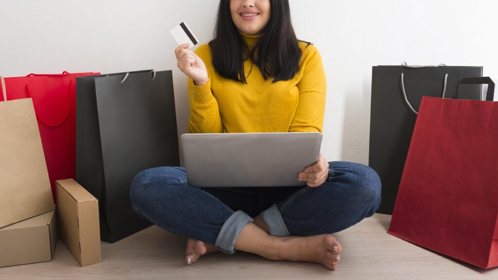 Woman with laptop and credit card surrounded by shopping bags