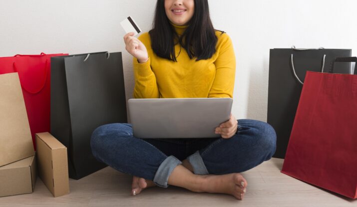 Woman with laptop and credit card surrounded by shopping bags