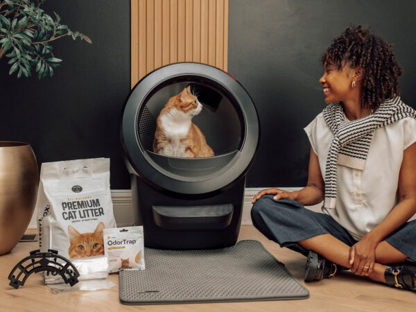 Woman sitting near cat in automated litter box