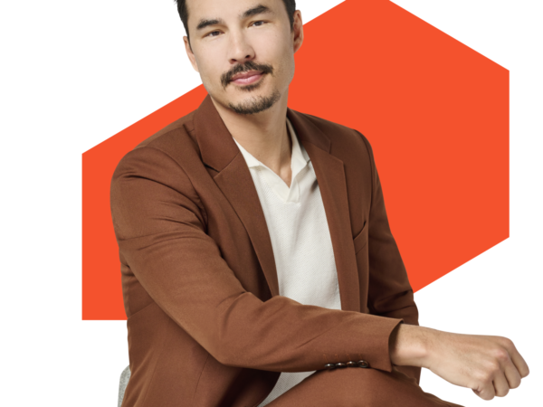 Man in brown suit seated with orange background