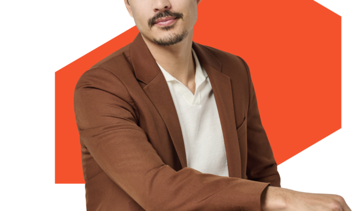 Man in brown suit seated with orange background
