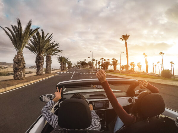 Couple driving convertible palm-lined road sunset