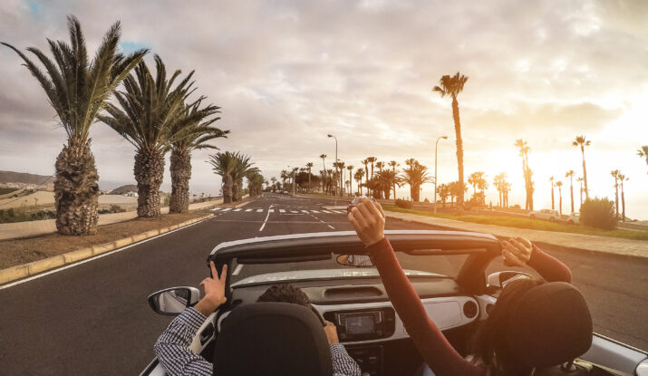 Couple driving convertible palm-lined road sunset