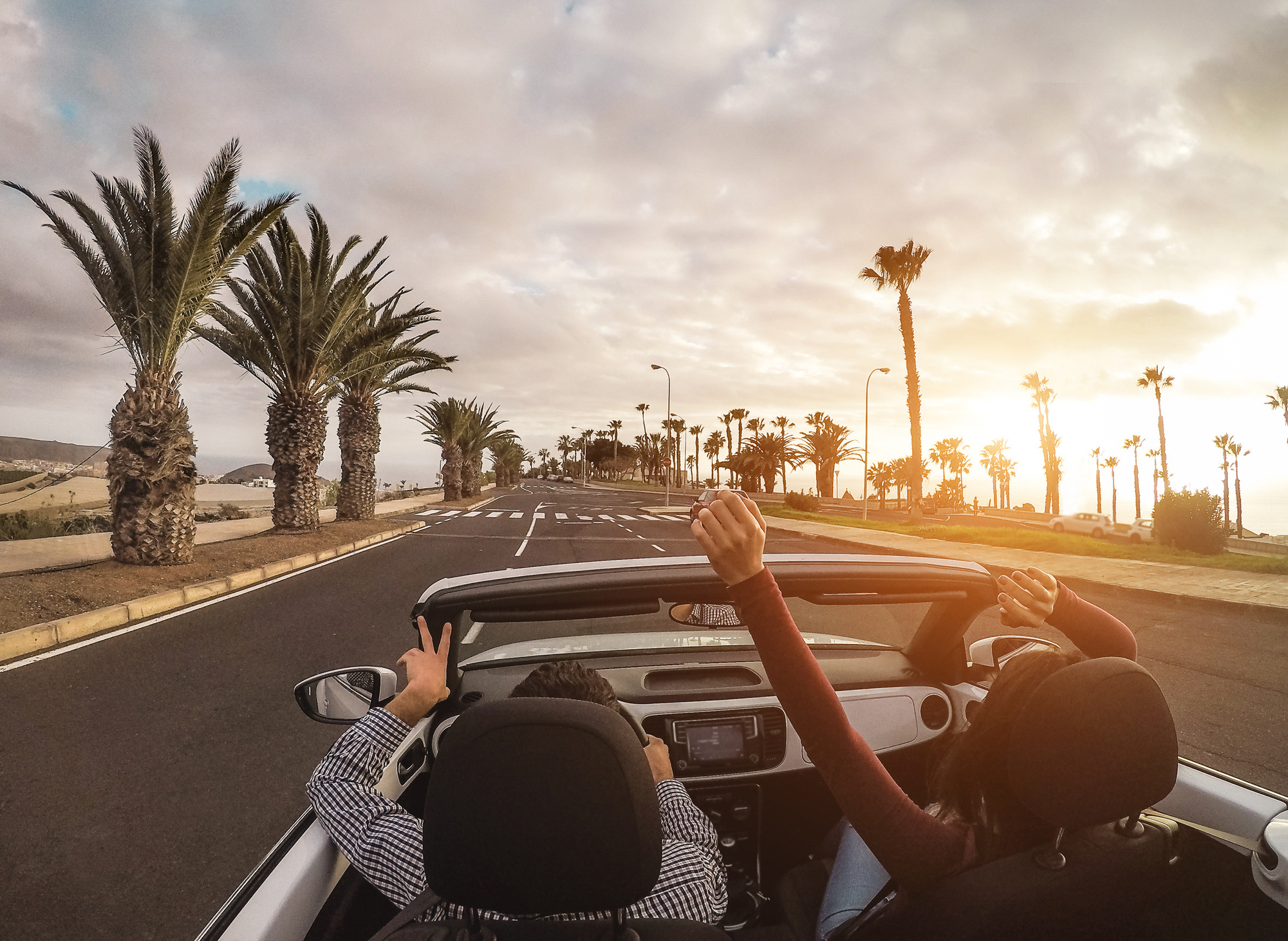 Couple driving convertible palm-lined road sunset