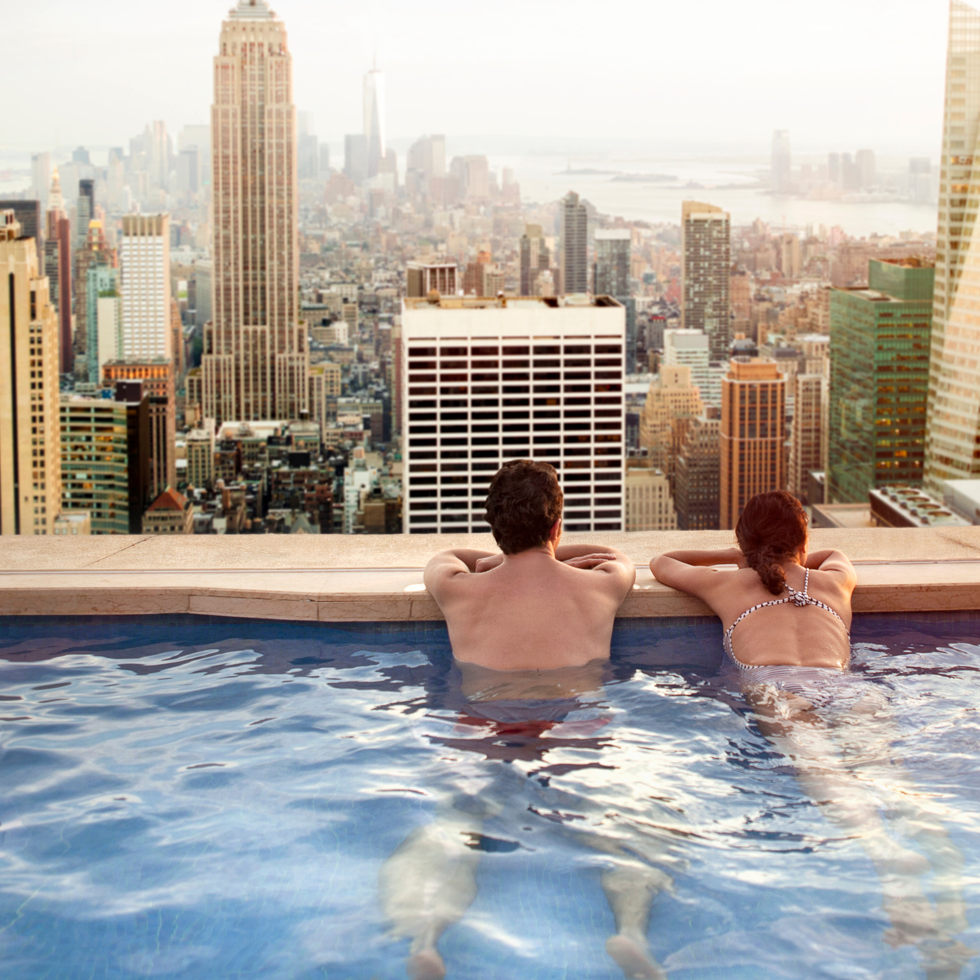 Two people relaxing in rooftop pool overlooking city skyline