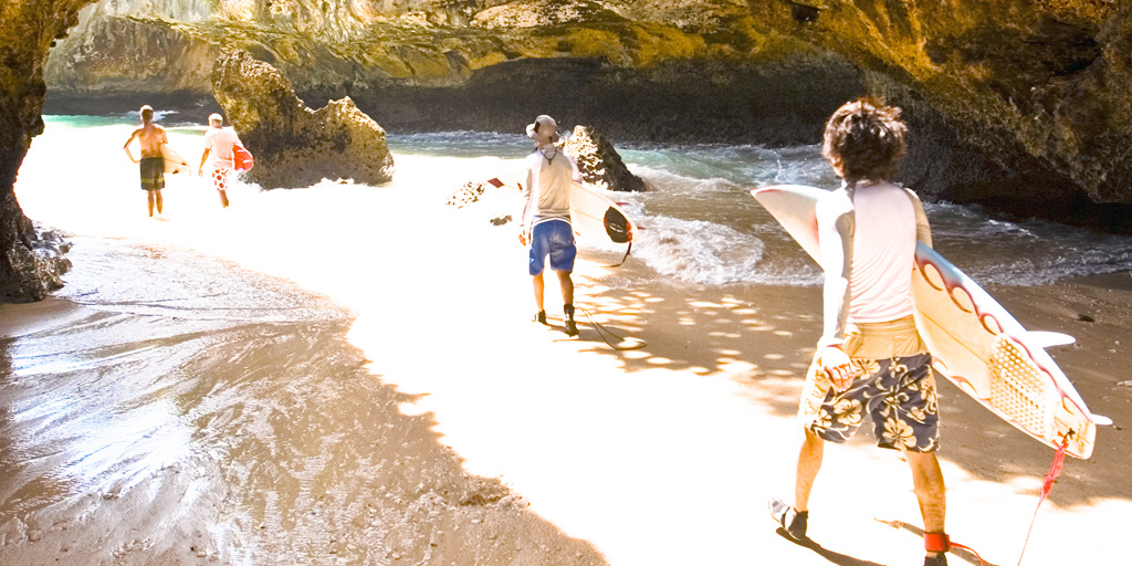 Surfers carrying boards walking through sunlit coastal cave