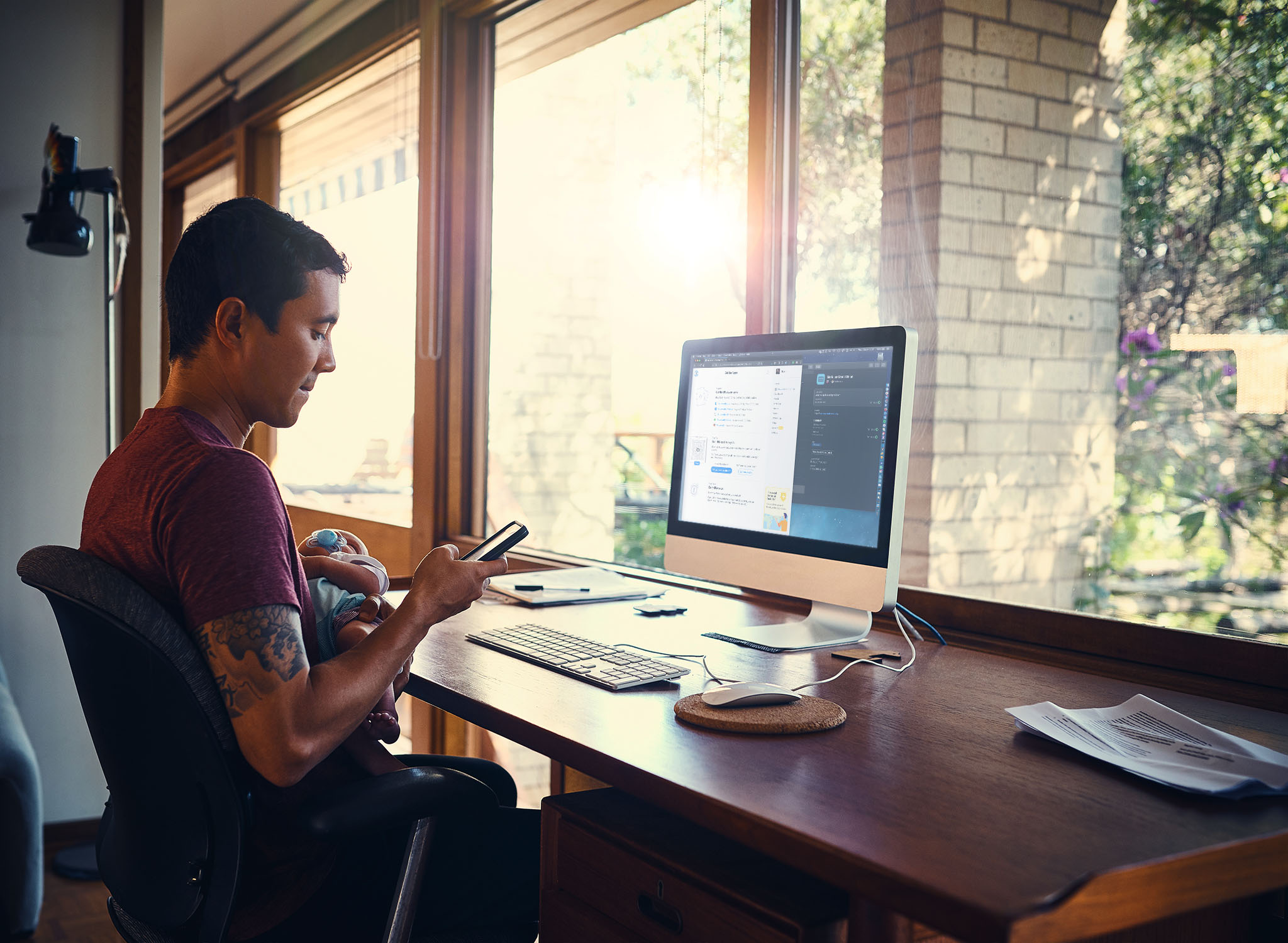Man holding baby while using phone at desk