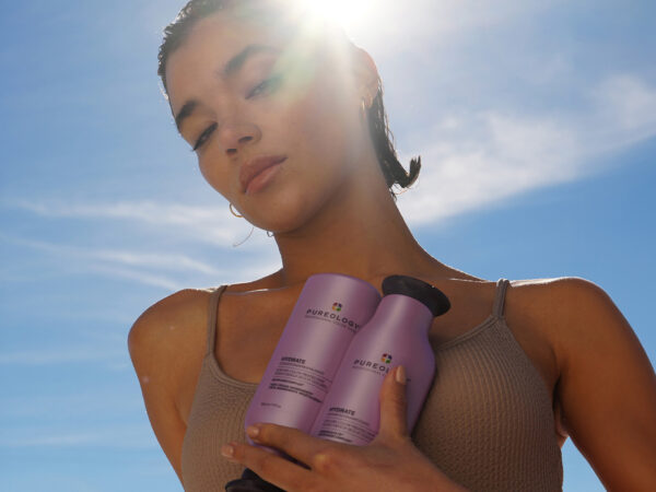 Woman holding Pureology Hydrate hair care bottles under sunlight