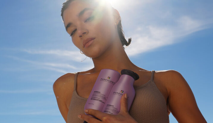 Woman holding Pureology Hydrate hair care bottles under sunlight