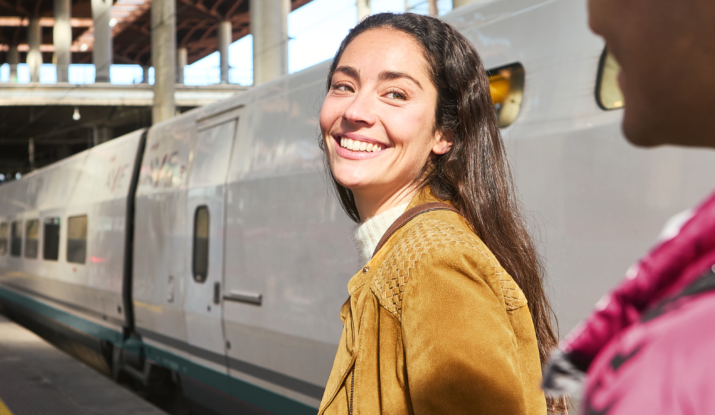 Smiling woman with suitcase standing by train platform