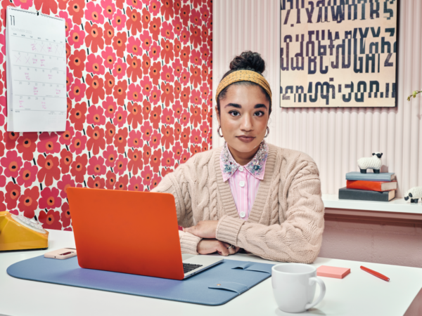 Woman sitting at desk with orange laptop and floral wallpaper