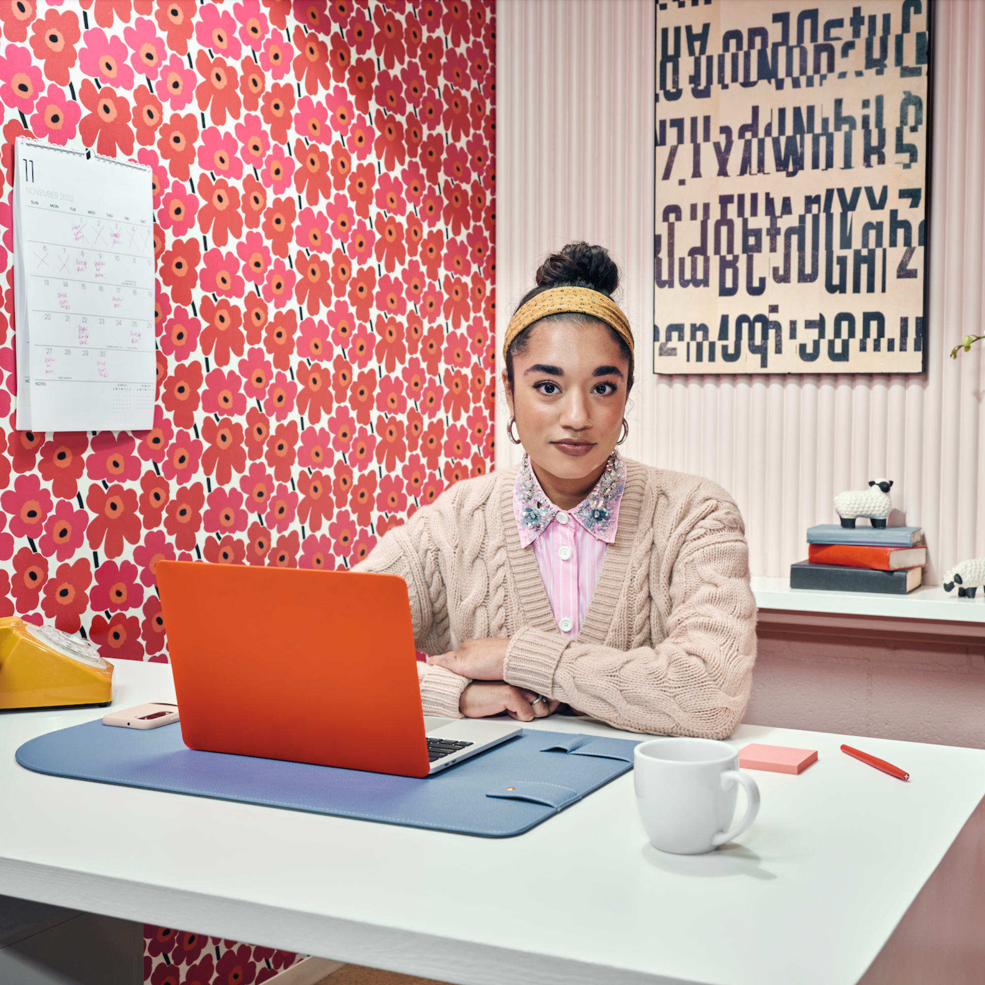 Woman sitting at desk with orange laptop and floral wallpaper