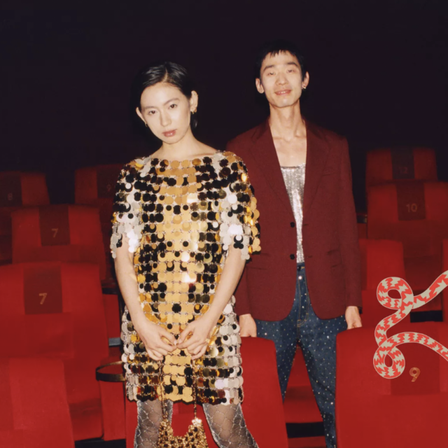 Two fashionably dressed people standing among red theater seats