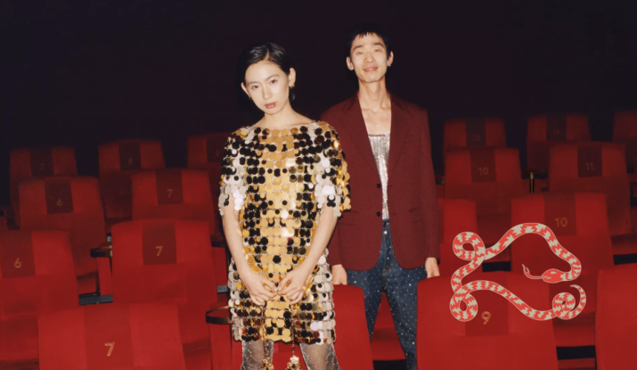 Two fashionably dressed people standing among red theater seats