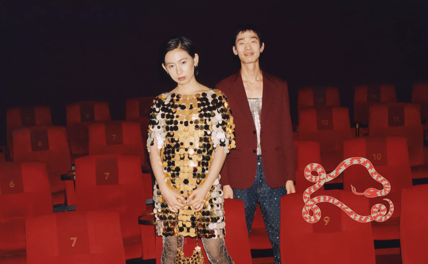 Two fashionably dressed people standing among red theater seats