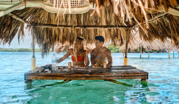 Couple eating under thatched hut in shallow water