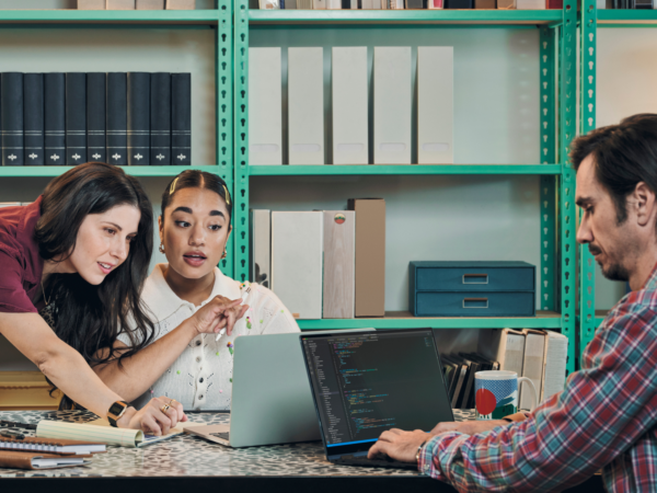 Three colleagues collaborating on laptops at office table