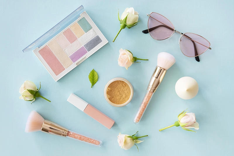 Makeup products, brushes, flowers, sunglasses flat lay