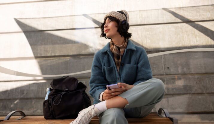 Young woman listening music outdoors, holding phone