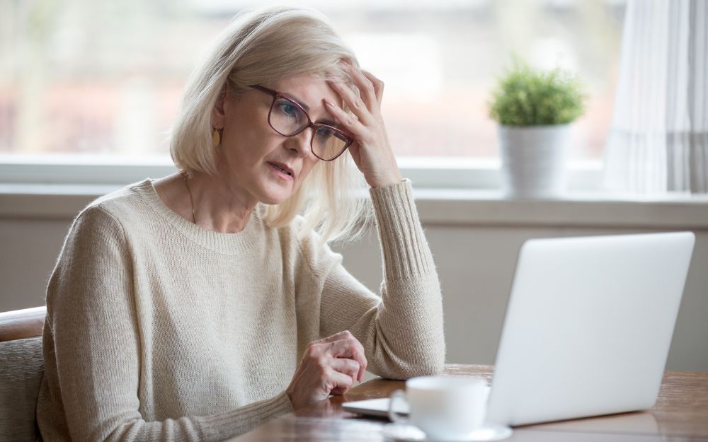 Worried woman using laptop with hand on forehead