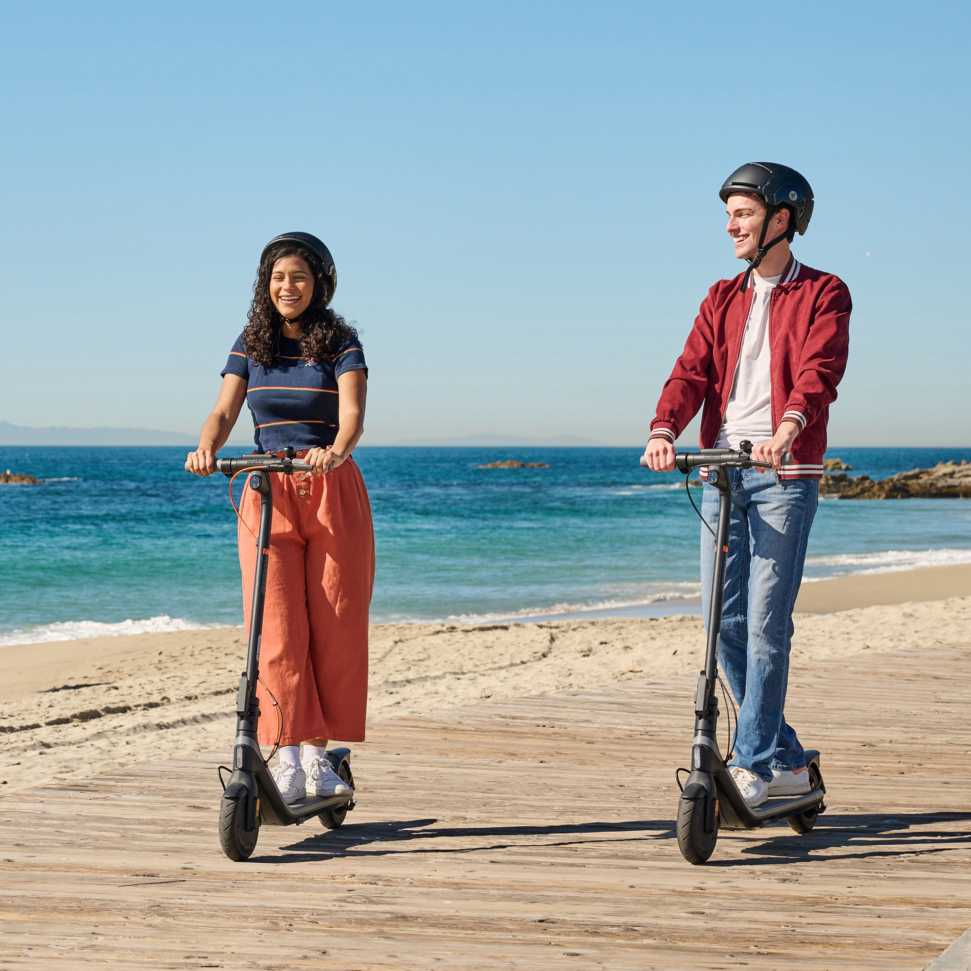 Young man and woman riding electric scooters by beach