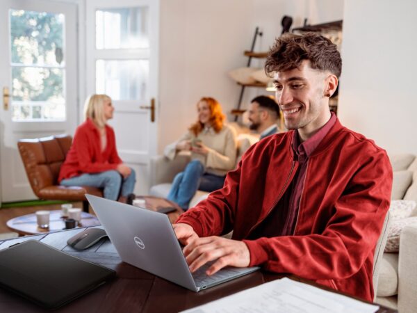 Young man typing on laptop with group chatting in background