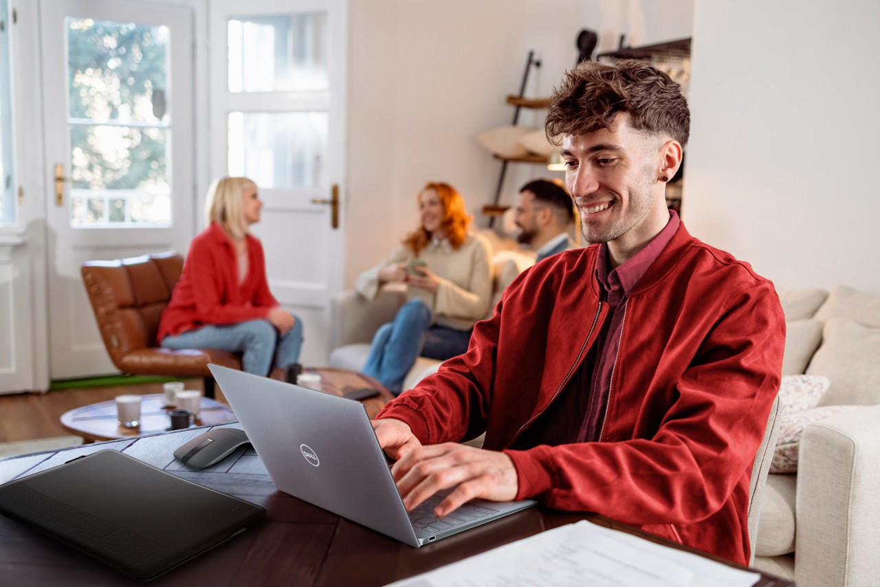 Young man typing on laptop with group chatting in background